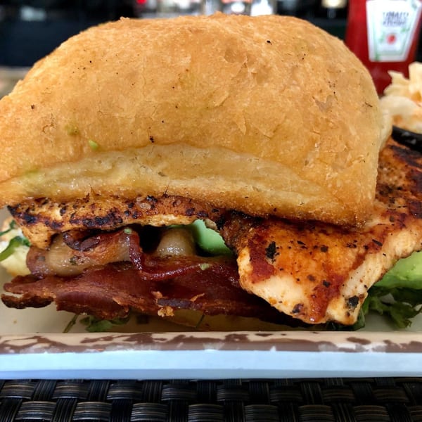 Close-up of a grilled chicken sandwich with bacon, avocado, and caramelized onions on a bun.