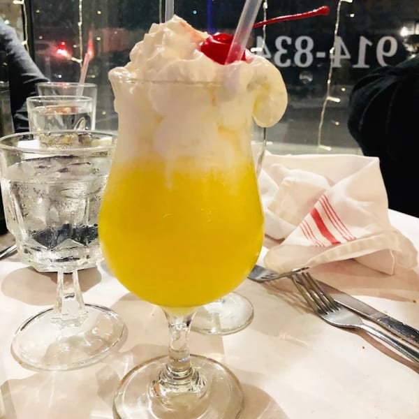 A vibrant yellow drink with whipped cream and a cherry, next to a water glass and napkin.