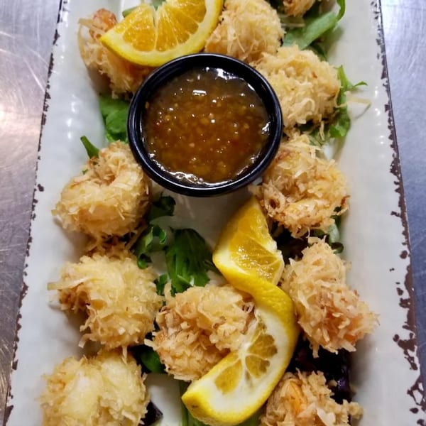 Coconut shrimp appetizer with orange slices and a dipping sauce on a rectangular white plate.