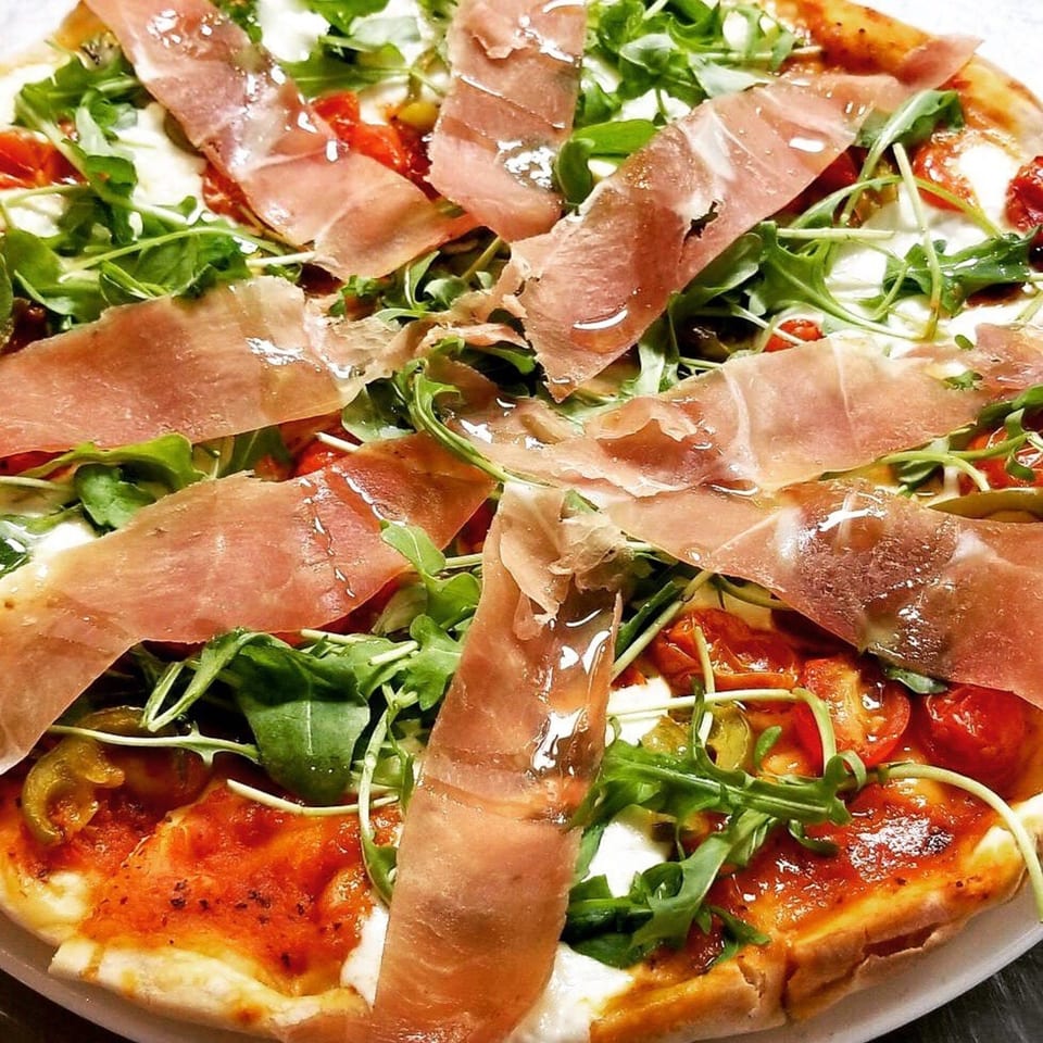 Augie's Italian pizza topped with prosciutto, fresh arugula, cherry tomatoes, and mozzarella.