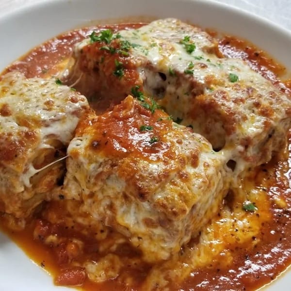 Three cheesy lasagna rolls in a rich red tomato sauce, garnished with fresh parsley.