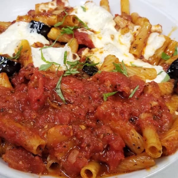 Close-up of baked ziti with rich red sauce, melted mozzarella, black olives, and fresh basil.