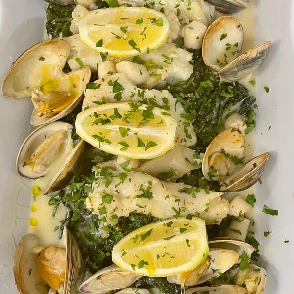 Clams, scallops, and white fish in a creamy sauce with spinach, parsley, and lemon slices.