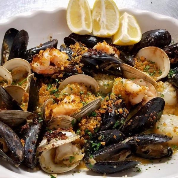 A white platter filled with mussels, clams, shrimp, and scallops, garnished with lemon wedges.
